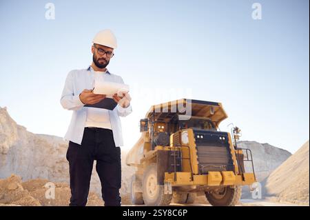 Smart person is with documents in hands. Man in uniform is working in the quarry at daytime. Stock Photo