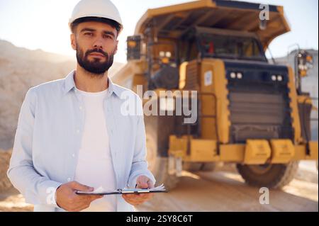Smart person is with documents in hands. Man in uniform is working in the quarry at daytime. Stock Photo