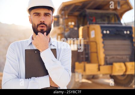 Smart person is with documents in hands. Man in uniform is working in the quarry at daytime. Stock Photo