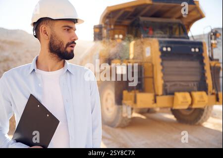 Smart person is with documents in hands. Man in uniform is working in the quarry at daytime. Stock Photo