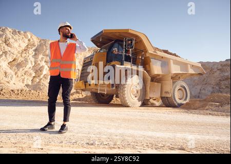 Using smartphone. Man in uniform is working in the quarry at daytime. Stock Photo