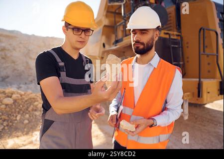Checking rock that is in the hands. Two men in uniform are working together in the quarry. Stock Photo