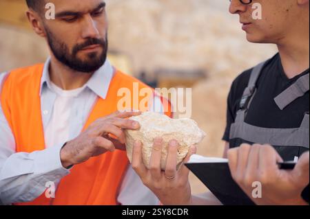 Checking rock that is in the hands. Two men in uniform are working together in the quarry. Stock Photo