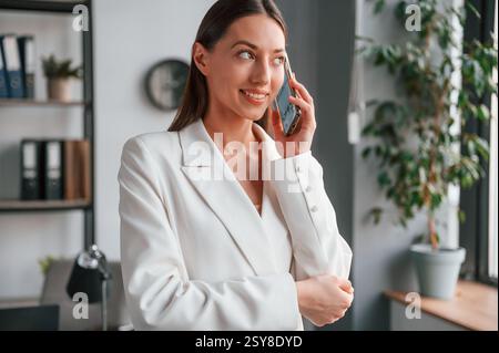 Talking by phone. Young beautiful woman in formal clothes is working at office. Stock Photo
