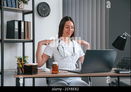 Doing online consultation. Young beautiful female doctor in white coat is in the office. Stock Photo