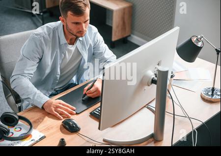 Top view. Designer is sitting by the computer and using graphics tablet with stylus. Stock Photo