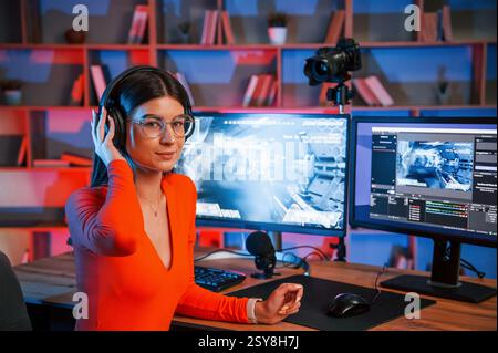 Wearing headphones. Young beautiful game streamer is indoors with pc. Stock Photo