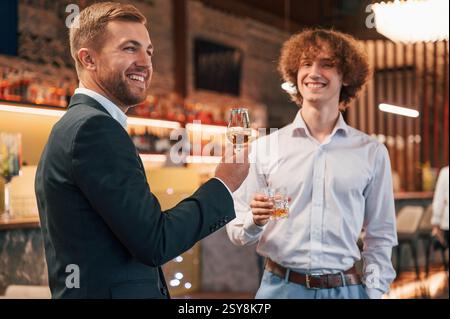 Two men are standing at the party together with alcohol drinks in hands. Stock Photo