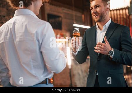 Two men are standing at the party together with alcohol drinks in hands. Stock Photo