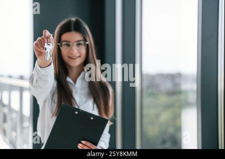 Happy young woman is holding keys for the new apartment. Standing on the construction site. Stock Photo