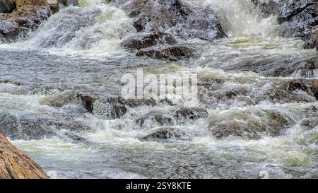 Close-up of fast-moving river rapids cascading over rocks, showing churning white water and natural motion. Stock Photo