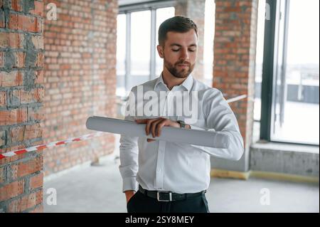 Checking the time. Man in white shirt is working indoors at construction site. Managing the project. Stock Photo