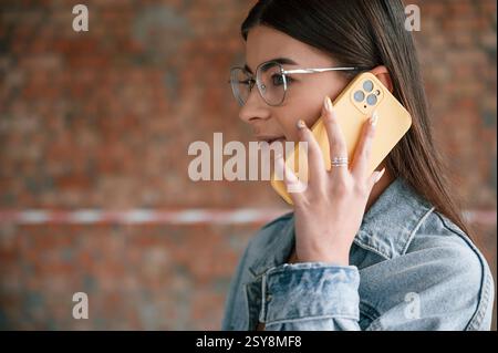 Talking by phone. Young woman is standing in the unfinished building on construction site and working on a project. Stock Photo