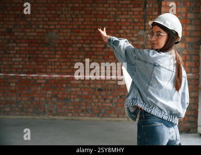 Young woman is standing in the unfinished building on construction site and working on a project. Stock Photo