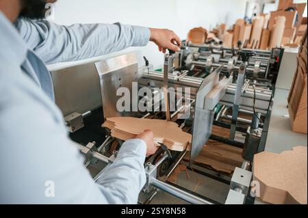 Operating printing cutting machine. Print house worker in white clothes is indoors. Stock Photo