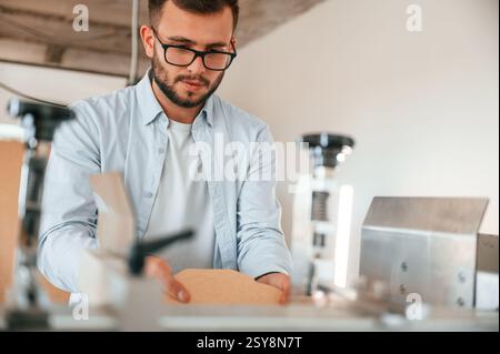 Using the cutting machine. Print house worker in white clothes is indoors. Stock Photo