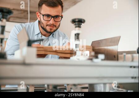 Using the cutting machine. Print house worker in white clothes is indoors. Stock Photo