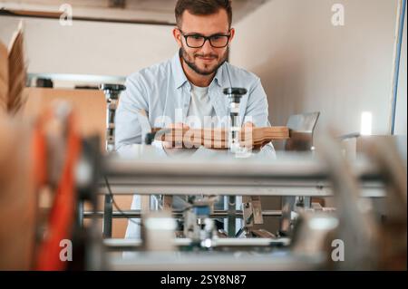 Using the cutting machine. Print house worker in white clothes is indoors. Stock Photo
