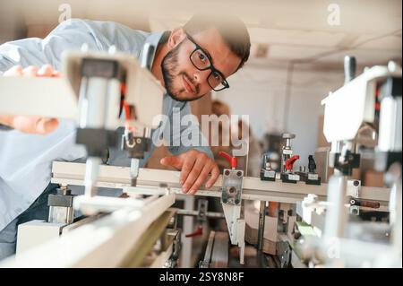 Using the cutting machine. Print house worker in white clothes is indoors. Stock Photo