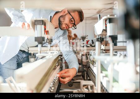 Process of using the cutting machine. Print house worker in white clothes is indoors. Stock Photo