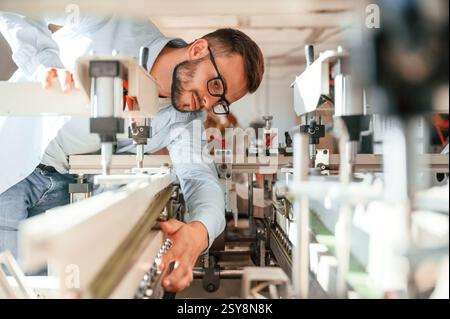 Process of using the cutting machine. Print house worker in white clothes is indoors. Stock Photo