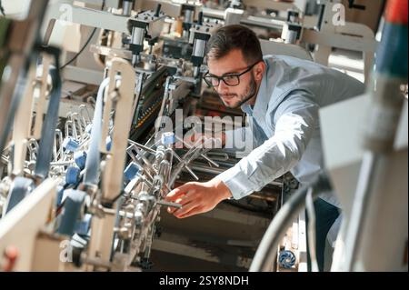 Setting up a printing machine. Typography worker in white clothes is indoors. Stock Photo