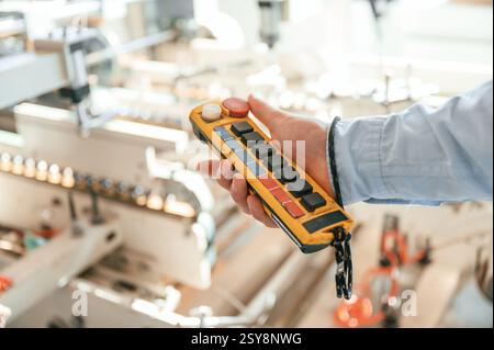 Holding controller of printing machine. Polygraph worker in white clothes is indoors. Stock Photo