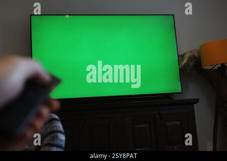 green screen tv. man holding remote control turning on tv changing channels. green screen for editing. Stock Photo