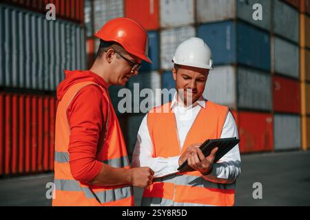 Using digital tablet. Two male workers is on the location with containers. Stock Photo