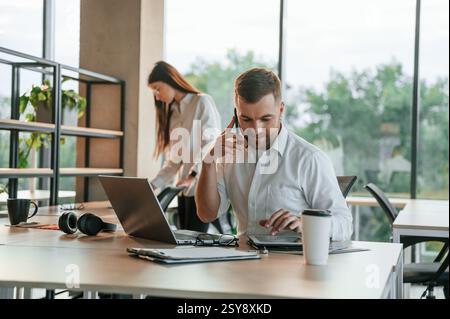 Boss is having conversation by the phone. Man and woman are working in the modern office together. Stock Photo