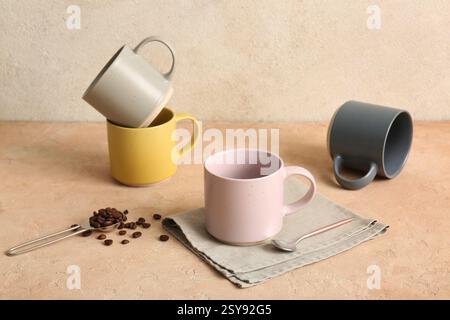 Ceramic mugs, napkin and teaspoon with coffee beans on pink table near light wall Stock Photo