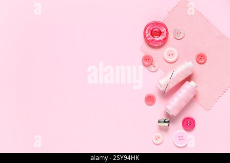 Different colorful buttons with thread spools and fabric sample on pink background Stock Photo