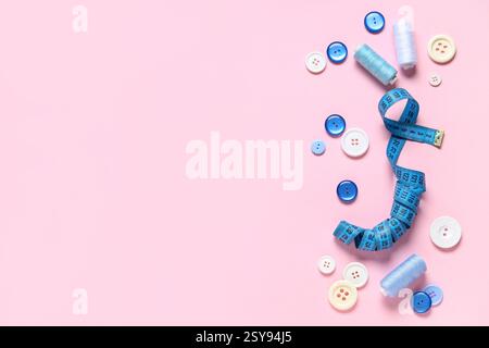 Different colorful buttons with thread spools and measuring tape on pink background Stock Photo