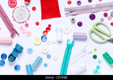 Different colorful buttons with thread spools, zippers, ball pins and scissors on white background Stock Photo