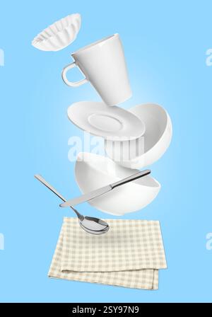 Clean dishware and silverware flying over checkered napkin on light blue background Stock Photo