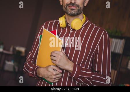 Young bearded man with headphones holding notebooks indoors, showcasing casual style and readiness for education Stock Photo