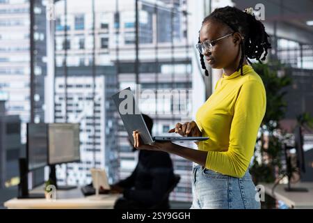 Cybersecurity expert using laptop to look for company security vulnerabilities, comparing with computer monitors. Programmer installing fortified code on laptop, crosschecking with PC screens Stock Photo
