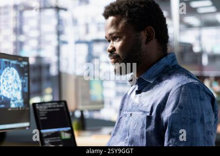 Cheerful employee utilizing AI cloud computing resources and platforms to train and deploy large scale machine learning models. Smiling african amertican man monitoring and maintaining company systems Stock Photo