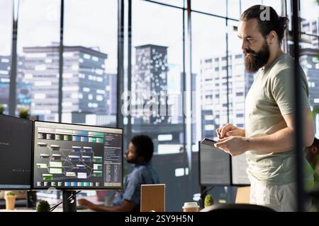 Technician using device for managing cloud computing resources and platforms to train large scale machine learning models. Man in office monitoring and maintaining company systems using tablet Stock Photo