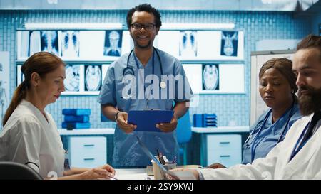 Licensed nurse specialist meeting with team for a research session, personalized medical services. Group of diverse healthcare professionals collaborating on treatment plans in a clinic. Camera B. Stock Photo