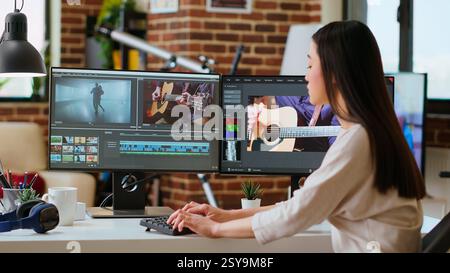 Asian woman edits videos in a creative software at her home office. Filmmaker using dual monitors and color wheel to work on footage in post production, highlighting remote work lifestyle. Camera B. Stock Photo