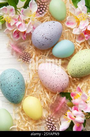 Pastel colored easter eggs with spring flowers and feathers creating a frame on white wooden background with copy space Stock Photo