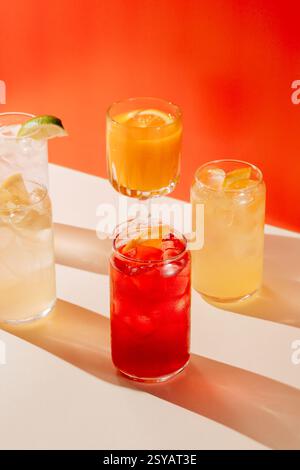 A vibrant assortment of lemonades and juices, each served in a distinct glass. The drinks feature slices of citrus and ice, set against a warm orange Stock Photo