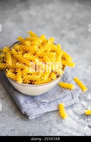 A rustic bowl filled with uncooked cavatappi pasta sits atop a folded linen napkin on a textured gray surface, capturing simplicity and inviting culin Stock Photo