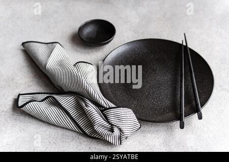 A sophisticated black and white table setting with a round black plate, chopsticks, and a striped napkin, presenting a minimalist and elegant dining t Stock Photo