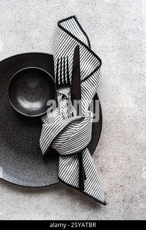 A minimalist black and white table setting featuring a sleek black plate, bowl, and cutlery, complemented by a folded striped napkin. Perfect for eleg Stock Photo