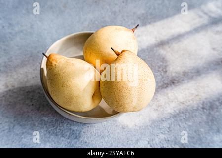 Three Chinese white pears in a bowl are placed on a textured surface. The pears' smooth, speckled skin contrasts with the rough background, capturing Stock Photo