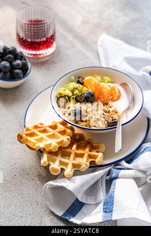 A nutritious breakfast bowl with yogurt, granola, fresh kiwi, blueberries, and tangerine slices. Paired with golden waffles and a vibrant juice, perfe Stock Photo