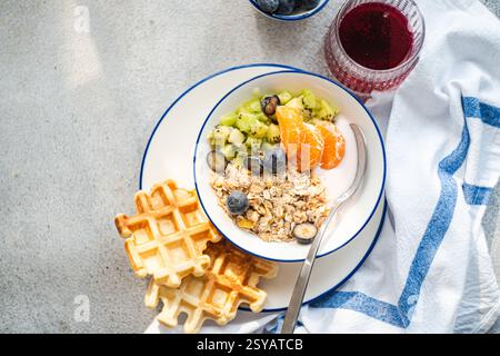 A delicious breakfast scene featuring granola with yogurt, kiwi, blueberries, orange slices, and waffles on a plate. A vibrant and nutritious start to Stock Photo