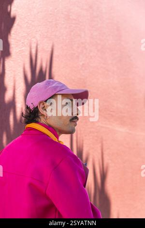 Young Spanish Caucasian man with a mustache, showcases a vibrant pink outfit that complements an urban lifestyle. He enjoys a day out in the city of Q Stock Photo